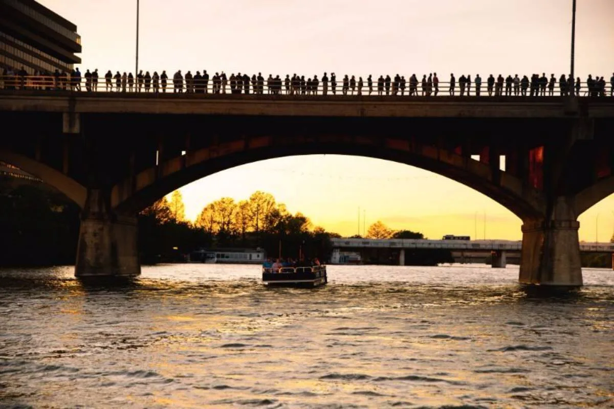 Bat-watching boat passing beneath Congress Avenue Bridge at sunset in Austin